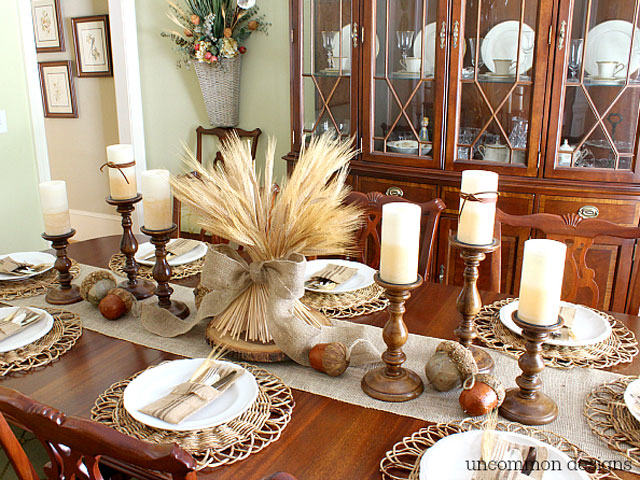 thanksgivingtablescapes: white china plates wheat grass tied with burlap for centerpiece and cream colored candles. acorns are scattered on the table runner