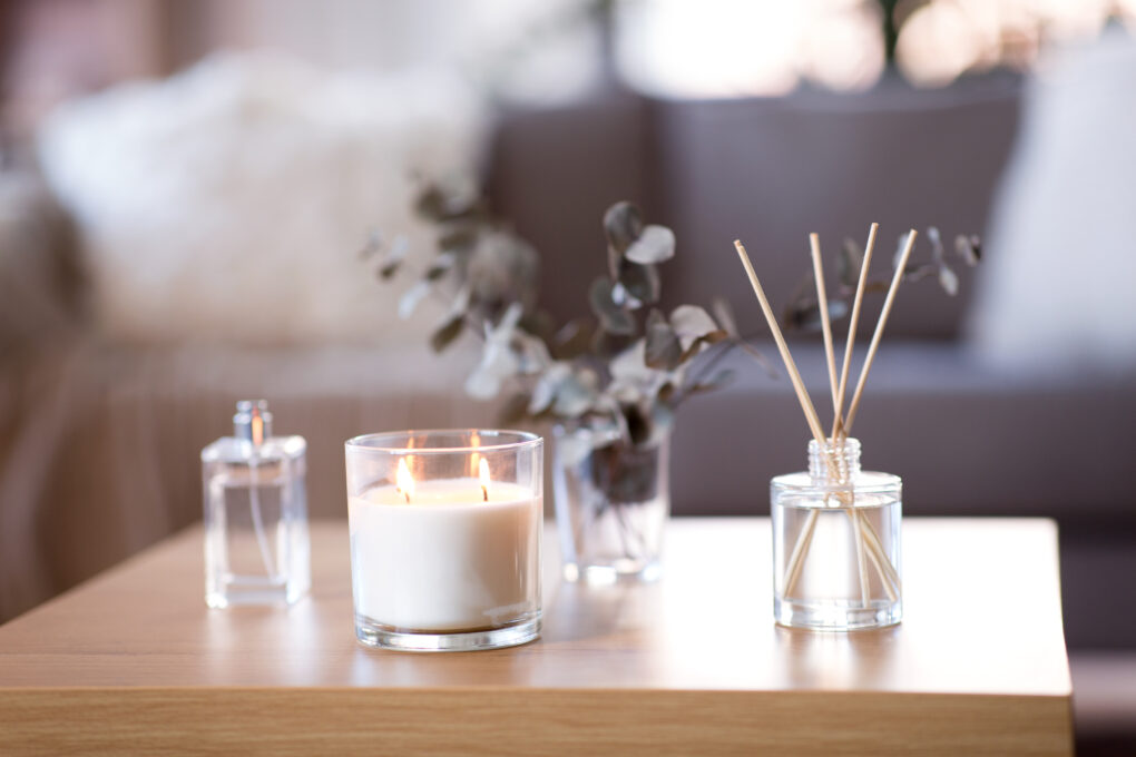A candle burning on a coffee table next to a reed diffuser.