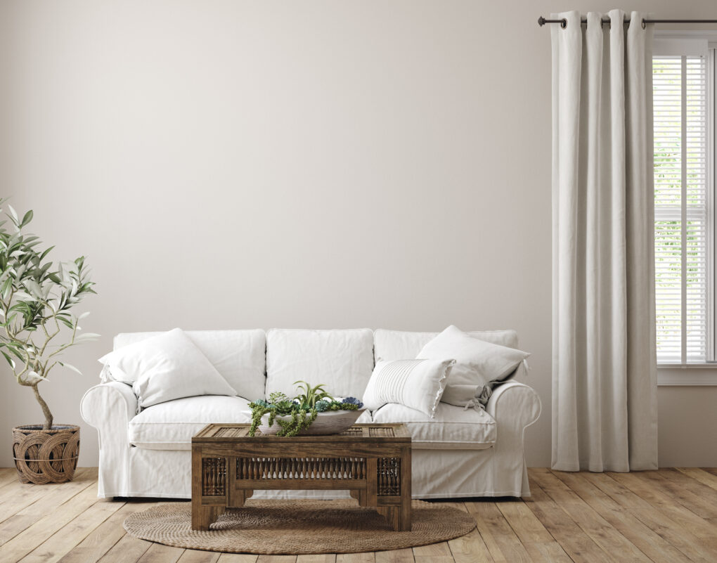 A farmhouse living room with a plant, couch, wooden table, wooden floors, and curtains.